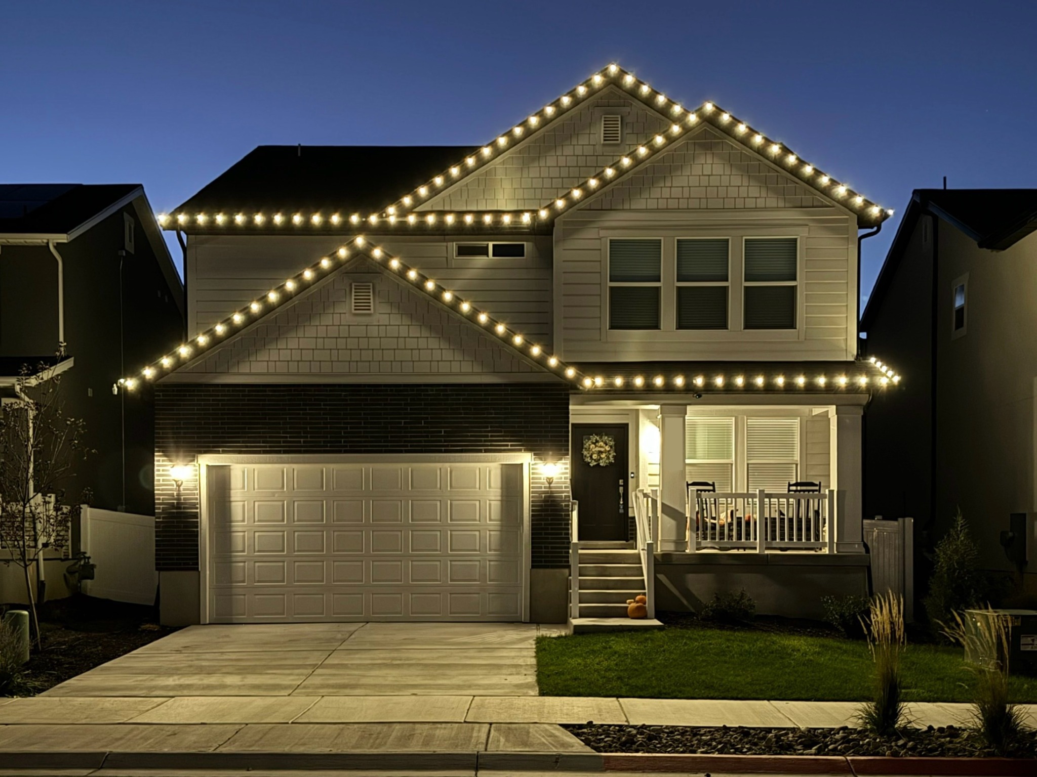Two-story home with warm white roofline lights against a blue evening sky