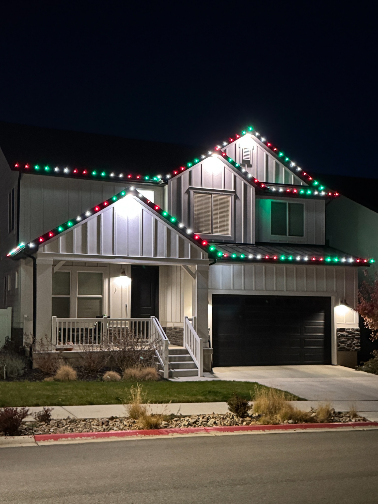 Two-story home with red, green, and pure white lights along its gabled rooflines