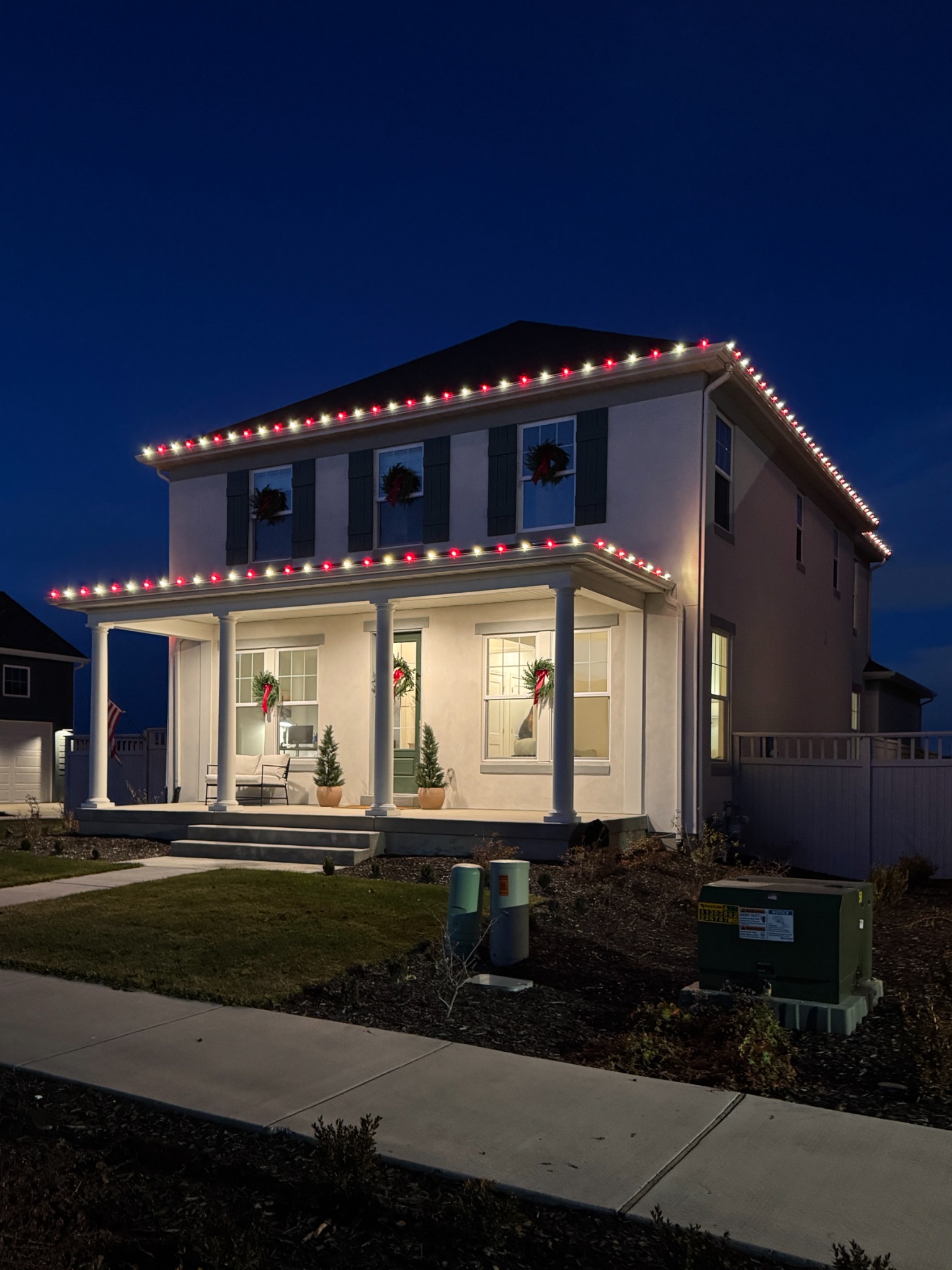 Two-story home with a columned porch and alternating red and warm white roofline lights