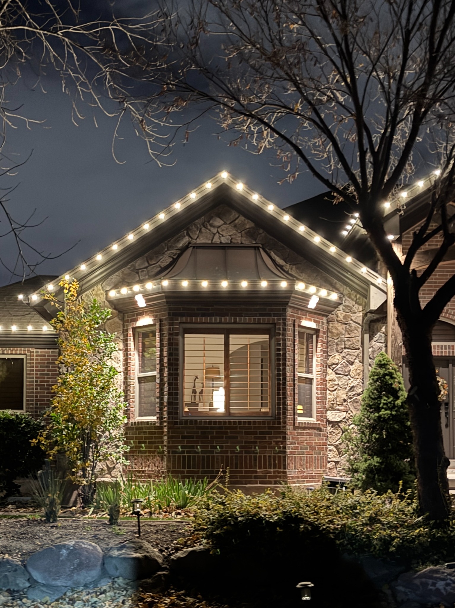 Warm white Christmas lights outlining a stone gable and bay window